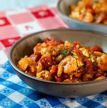 Bowl with shrimp and tomatoes on a checkered tablecloth.