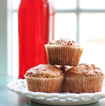 Stack of 3 cranberry muffins with cranberry liqueur in the background.