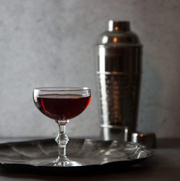Deep red cocktail on a silver plate with a cocktail shaker.