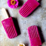 Three Bright pink popsicles with flowers on a tray.