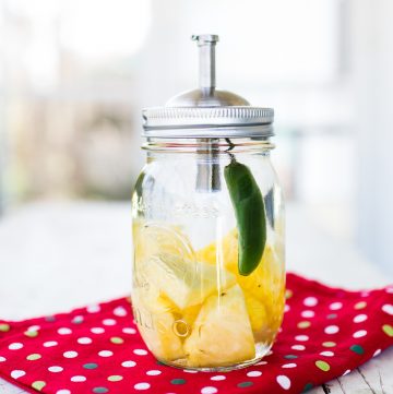 Mason. jar filled will with clear liquid and pineapple and jalapeno.