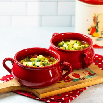 Two red bowls of soup topped wit avocado.