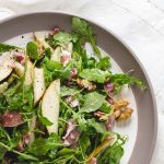 Plate with salad with arugula, pears, and walnuts.