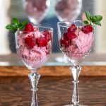 Two goblets filled with pink ice cream and topped with raspberries.