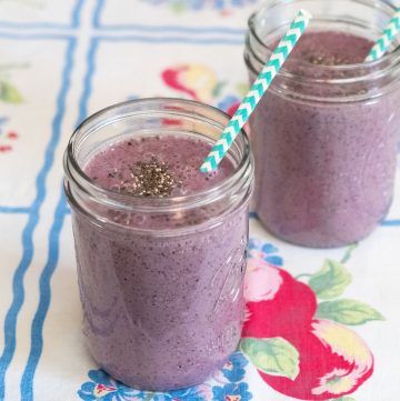 Two jars of blueberry smoothies with striped straws.