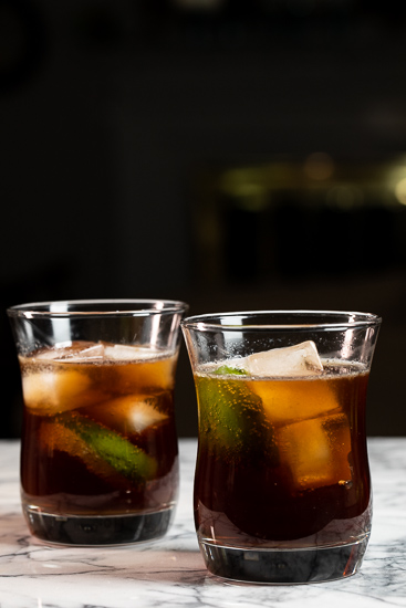 Two glasses filled with a Cuba Libre cocktail.