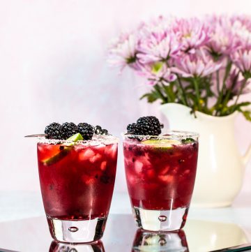 Two dark purple cocktails garnished with blackberries and rimmed with salt.