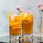 Two cocktails with a long lemon garnish.