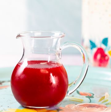 Small pouring pitcher with bright red syrup inside.