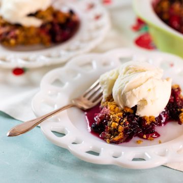 White plate with berry crisp topped with ice cream.