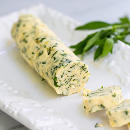 White plate with herb butter sliced on it.