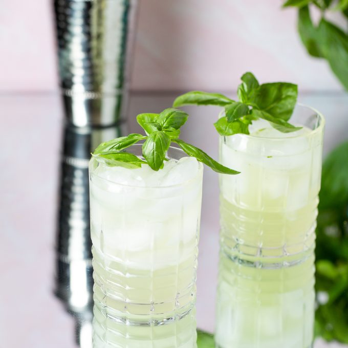 Two pale green cocktails garnished with basil.