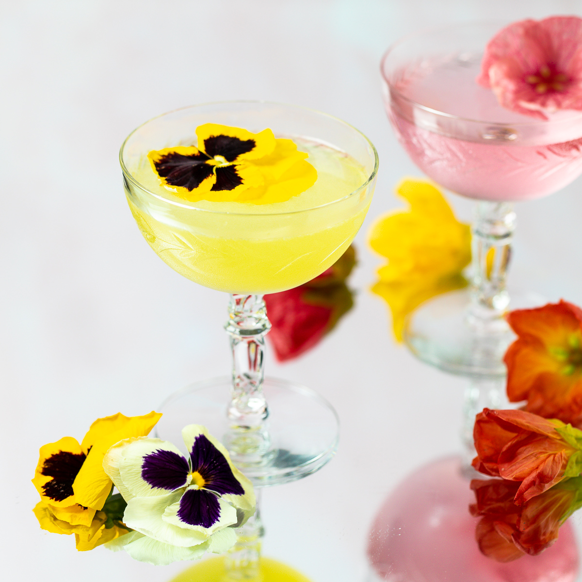 Bright yellow cocktail garnished with a pansy flower.