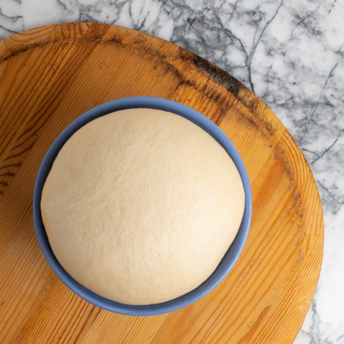 Pizza dough in a bowl on a wooden pizza peel.