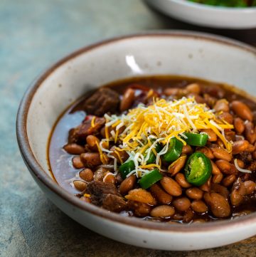 Bowl of beans topped with cheese and jalapeño peppers.