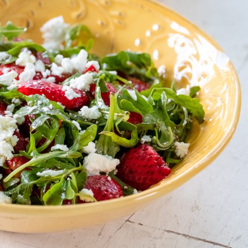 Arugula, strawberries and goat cheese in a yellow bowl.