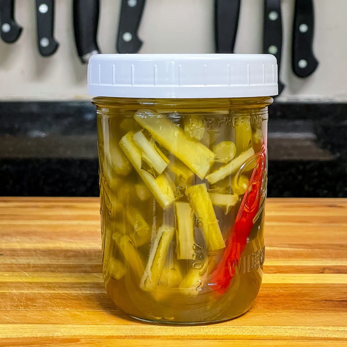 Mason jar with white lid and pickled collard stems in the jar.