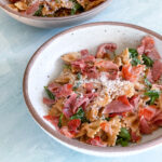 Bowl of pasta with prosciutto and arugula topped with parmesan cheese.