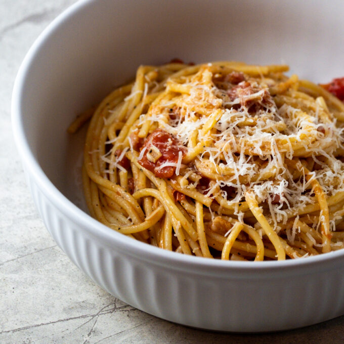 Close up of a bowl of pasta amatriciana topped with shredded cheese.