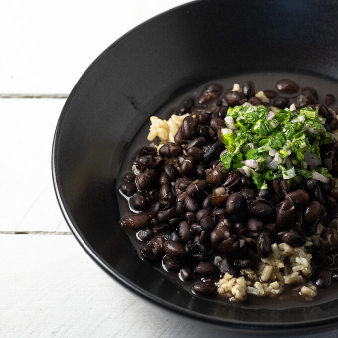 Close up of a bowl of black beans topped with cilantro salsa.