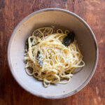 Bowl of pasta with crispy sage leaves and parmesan cheese on top.
