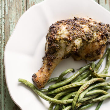 Roast chicken with tarragon pesto on a plate with green beans.